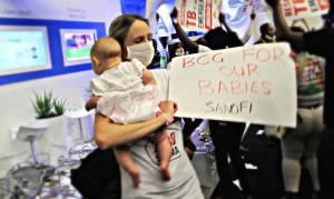 New mother Dr Dalene von Delft joins the Treatment Action Campaign in storming the stand of French multinational pharmaceutical company Sanofi. Delft, a multidrug-resistant tuberculosis (TB) survivor, holds a placard demanding the company ensures adequate supplies of its childhood TB vaccine are available worldwide.